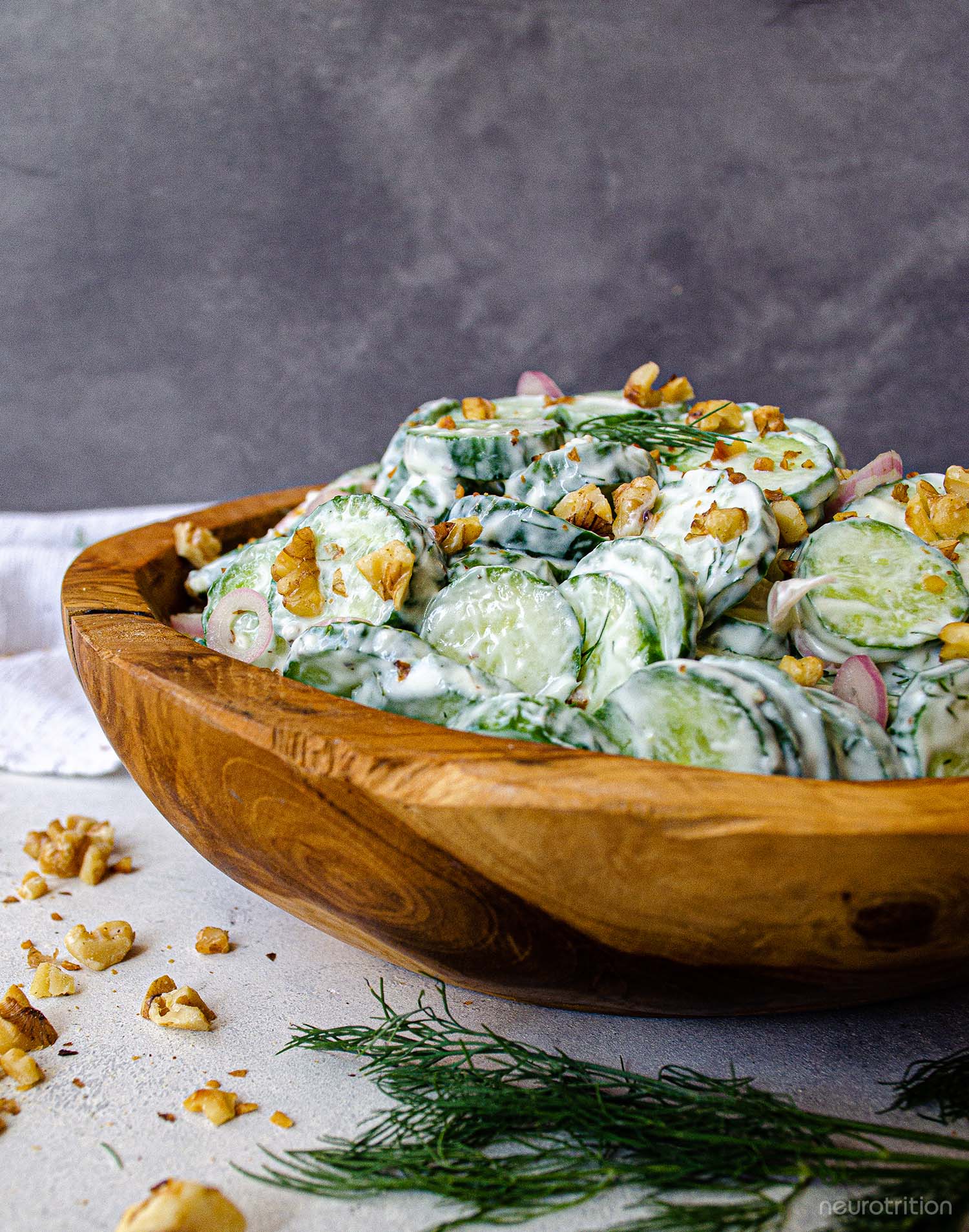 Creamy Cucumber Salad Sliced cucumbers and chopped walnuts in a creamy dressing inside a wooden bowl, topped with dill springs.