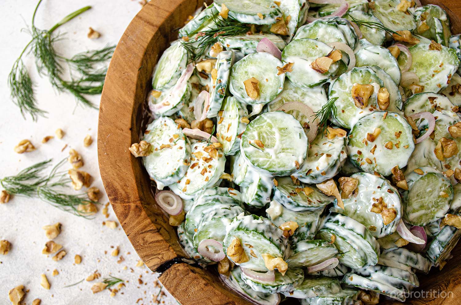 Creamy Cucumber Salad Sliced cucumbers and chopped walnuts in a creamy dressing inside a wooden bowl, topped with dill springs.