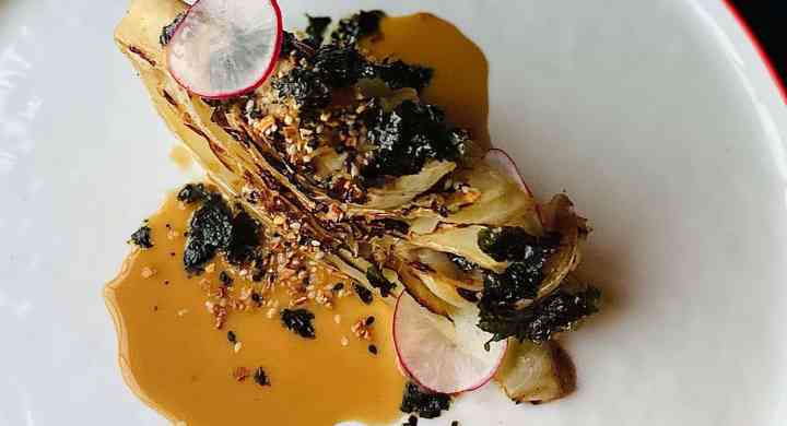 Charred cabbage with almond coconut yogurt sauce & seaweed furikake on a white plate with red trim