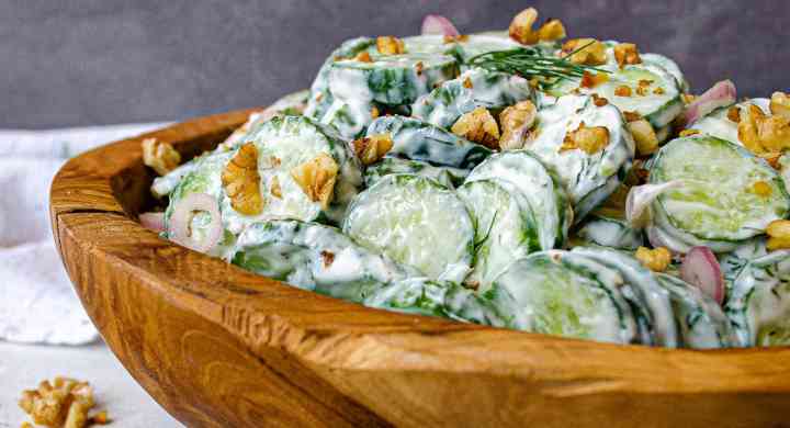 Creamy Cucumber Salad Sliced cucumbers and chopped walnuts in a creamy dressing inside a wooden bowl, topped with dill springs.