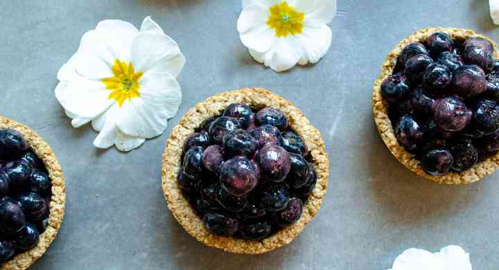 Fresh Mini Blueberry Pie Recipe Looking down on six mini blueberry pies placed in a grid with little white and yellow flowers in between the pies.