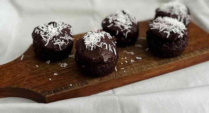 Fudgy chocolate cupcakes with sweet potato frosting topped with shredded coconut on wooden cutting board.